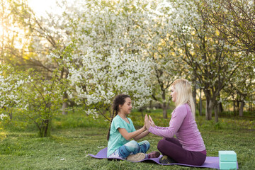Fototapeta premium Family Mother teacher training yoga child daughter on a yoga mat at home garden. Family outdoors. Parent with child spends time together. exercise at home concept and new normal.