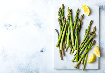 Bunch of fresh green asparagus on marble board. Green asparagus seasonal spring cooking. Overhead view, white background - obrazy, fototapety, plakaty