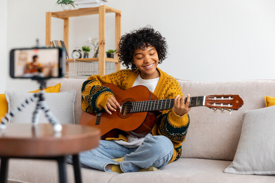Blogger guitarist. Happy african american girl blogger playing guitar singing song recording vlog. Social media influencer woman streaming recording at home studio. Music content creator broadcast