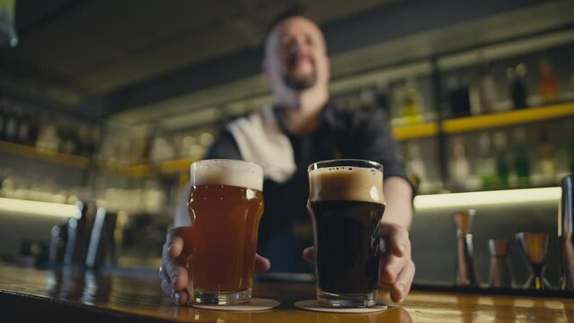 A bartender puts two glasses of beer on the bar in a pub. Party in a bar with friends with dark beer and ale. High quality 4k footage