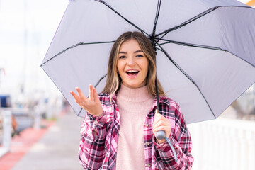 Young pretty Romanian woman holding an umbrella at outdoors with shocked facial expression