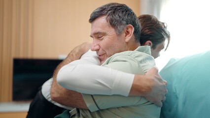 Happy son visits recovering old father lying on the bed in hospital. They lovingly embrace and smile. Elderly people healthcare concept