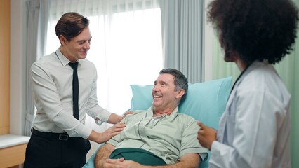 Obraz premium A happy son visits a recovering old father lying on the bed in hospital. and they talked with doctor