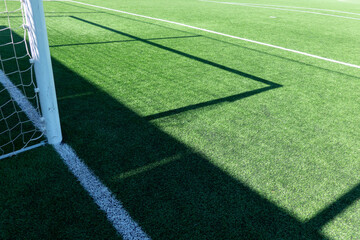 Artificial turf on football soccer field. Part of soccer goal and green synthetic grass on sport ground with shadow from goal net