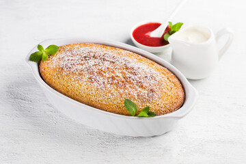 Freshly prepared mannik, semolina pie in the form sprinkled with powdered sugar with sour cream and berry sauce on a light gray background