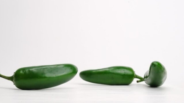 Whole green jalapeños falling and bouncing on white studio backdrop in 4k slow motion