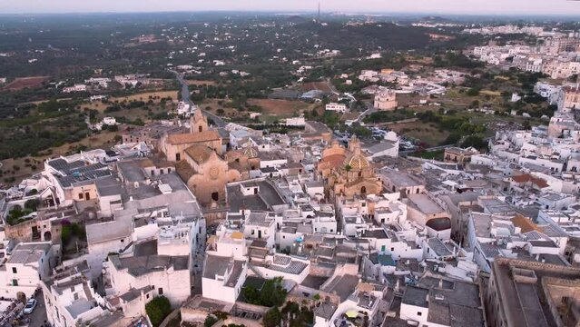 Aerial drone footage of Ostuni - La Citta Bianca (white city), Puglia, Italy at sunset. Reveal scene of Cathedral, Arco Scoppa, Porta Nova, the medieval historic old town tourist landmark from above