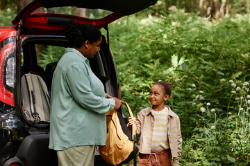 Side view portrait of African American mother and daughter standing by car in nature trail