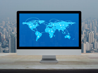 Connection line with global world map on computer monitor screen on wooden table over city tower...