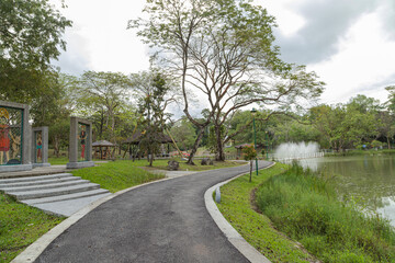 City park in Kuching, Malaysia, tropical garden with large trees and lawns, path, lake.