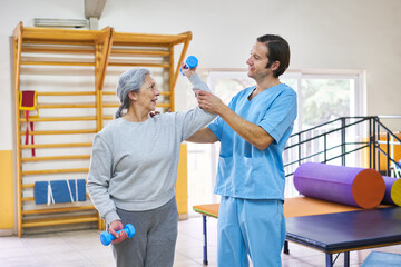 Fototapeta premium Caregiver assisting elderly woman exercising with dumbbells