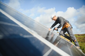Male worker in uniform outdoors with solar batteries at sunny day.
