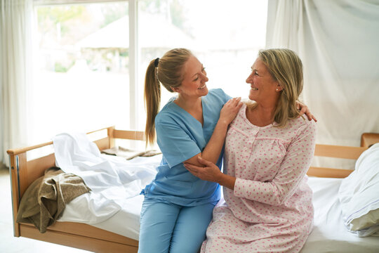 Smiling nurse embracing senior woman on bed in nursing home