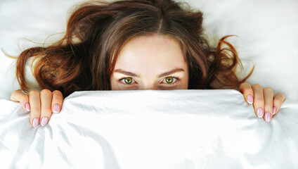 Woman in bed. Girl hides her face under the covers.Concept of healthy sleep, insomnia, comfort zone