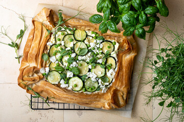 Zucchini and cheese phyllo dough tart with green peas, micro greens and basil. Zucchini and feta pizza, filo puff pastry. Savoury vegetable vegetarian baking.