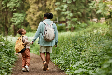 Back view of joyful mother and daughter walking on nature trail together holding hands, copy space