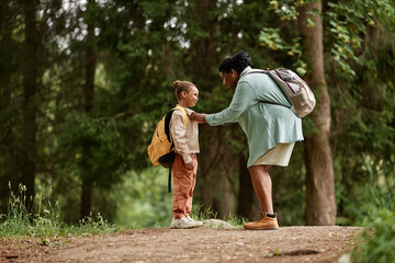 Side view portrait of black mother and daughter hiking together with backpacks and enjoying nature - obrazy, fototapety, plakaty