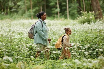 Side view portrait of mother and daughter walking across meadow while hiking in nature together