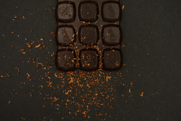 Bitter chocolate bar on a black paper background, close-up. View from above