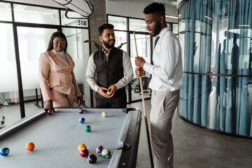 Young multiracial people in suits playing pool at office lobby
