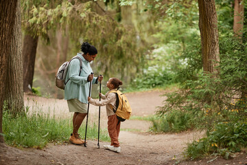 Side view portrait of black mother and daughter hiking together standing in beautiful forest trail,...