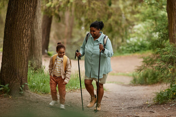 Full length portrait of black mother and daughter hiking together walking in beautiful forest...