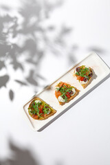 Aesthetic composition with salmon bruschetta on white background with shadows from flowers. Italian...