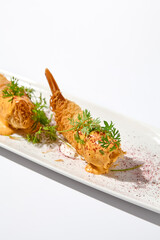 Traditional greek appetizer - kataifi wrapped shrimps on white plate. Crispy shrimp in kataifi crust in summer day. Shrimp appetizer fried in kataifi dough. Crispy prawns in modern style.