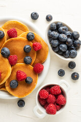 Flat lay of pancakes with blueberries and raspberries in bowls on white table, selective focus, vertical