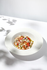 Elegant salad with smoked eel, strawberry and avocado on white table with harsh shadows. Eel salad with berries on white background with shadows of leaves. Romantic dining with fish appetizer.