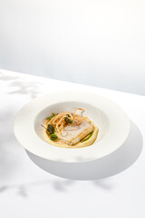 Roasted squid on mashed potatoes and crispy onion. Grilled squid with celery cream on white plate with shadows of leaves. Summer seafood menu. Roasted calamari in fine dining.