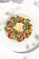 Homemade pasta with pastrami and creamy sauce with cheese. Italian pasta pappardelle with beef and sauce on white table Italian food in summer dining with shadows of sunlight