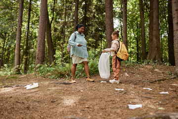 Side view portrait of mother and daughter picking plastic bottles on nature trail, copy space