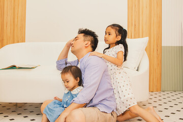 Father took care of his daughter until he was exhausted : Side view single father with two daughters in the living room taking a nap by the sofa as his mischievous daughter happily plays.