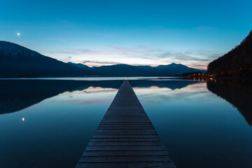 Obraz premium Wooden jetty on a lake at night with mountains in the background