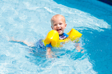 Baby with inflatable armbands in swimming pool.