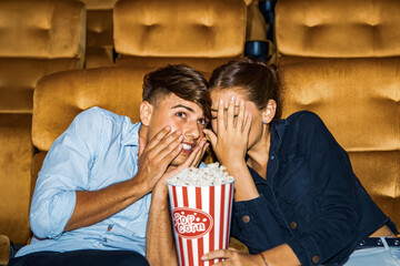 Caucasian couple holding popcorn sitting watching horror movie theater looking at a frightening...