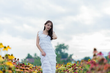 Beautiful Asian woman in garden with colorful flowers in foreground natural beauty while relaxing in the garden. Happy girl with flower field dress, travel concept.