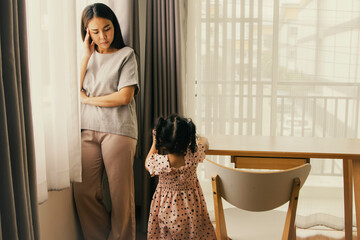 Stressed mother looks at little daughter worried about family problems sad all the time standing...