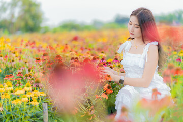 Naklejka na ściany i meble Beautiful Asian woman in garden with colorful flowers in foreground natural beauty while relaxing in the garden. Happy girl with flower field dress, travel concept.