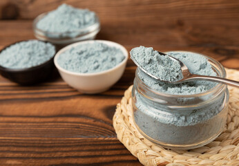 Blue spirulina powder in a bowl, jars and spoons on a brown wooden table. Natural vegan superfood. Healthy food supplement. Phycocyanin extract. Place for text. Place for a copy.