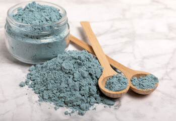 Blue spirulina powder in bowls and spoons on a marble table. Natural vegan superfood. Healthy food supplement. Phycocyanin extract. Place for text. Place for a copy.