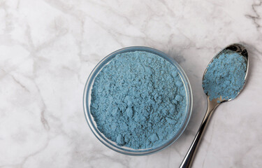 Blue spirulina powder in bowls and spoons on a marble table. Natural vegan superfood. Healthy food supplement. Phycocyanin extract. Place for text. Place for a copy.