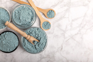 Blue spirulina powder in bowls and spoons on a marble table. Natural vegan superfood. Healthy food supplement. Phycocyanin extract. Place for text. Place for a copy.