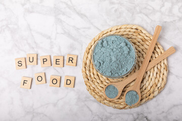 Blue spirulina powder in bowls and spoons on a marble table. Natural vegan superfood. Healthy food supplement. Phycocyanin extract. Place for text. Place for a copy.