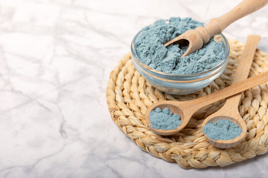 Blue spirulina powder in bowls and spoons on a marble table. Natural vegan superfood. Healthy food supplement. Phycocyanin extract. Place for text. Place for a copy.