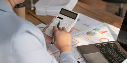 Business woman using calculator to calculate financial report, working at office with laptop...