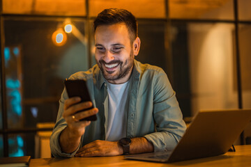 Happy businessman using a mobile phone while working over the laptop at the office.