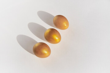 Three gold eggs diagonally on white background.