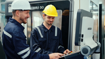 Two Caucasian production engineers in safety wear are discussing to plan for operating CNC machine...